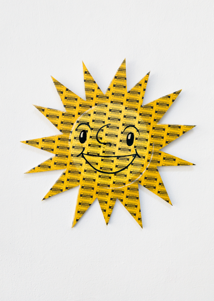 Flyer-Motiv zum Tisa-Preis 2026, den Jody Korbach in diesem Jahr gewinnen konnte. Es zeigt ein Sonnensymbol im Stil des Logos einer Spielbanken-Kette mit Smiley-Gesicht. Es ist angefertigt aus gelben Wertmarken. Foto: ©Johannes Bendzulla